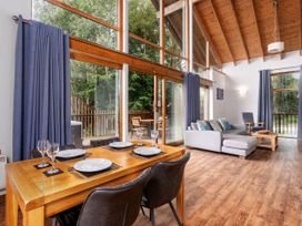 A dining table set with plates and glasses near large windows and a living area with a sofa and chair at Keldy Classic Silver Birch wheelchair accessible cabin in Keldy Forest