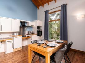 A kitchen with white cabinets a wooden dining table set for four and a large window with curtains at Keldy Classic Silver Birch wheelchair accessible cabin Keldy Forest