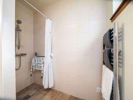 A bathroom with a wall-mounted shower chair a showerhead and towels on a heated rail at Keldy Classic Silver Birch wheelchair accessible cabin in Keldy Forest