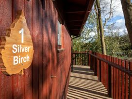 A wooden balcony with railing attached to a red wooden cabin with a wooden sign reading 1 Silver Birch Strathyre New Style Silver Birch wheelchair accessible cabin in Strathyre Ben Ledi