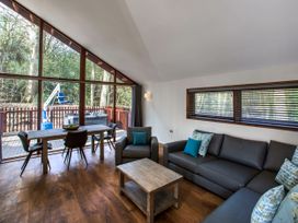 A living room with a sofa armchair coffee table dining table and chairs and large windows showing a deck with a hot tub at Strathyre New Style Silver Birch wheelchair accessible cabin Strathyre Ben Ledi