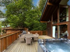 An outdoor wooden deck with a dining table and chairs a barbecue grill and a hot tub at Keldy Classic Golden Oak Treehouse in Keldy Forest