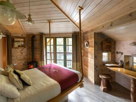 A wooden bedroom with a suspended bed a stove and a desk with a stool at Keldy Classic Golden Oak Treehouse in Keldy Forest