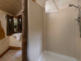A bathroom with a walk in shower a sink with a towel and a mirror framed with wood at Keldy Classic Golden Oak Treehouse in Keldy Forest