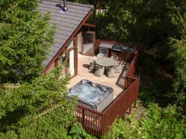 A wooden deck with a round table and chairs a hot tub and a barbecue grill surrounded by trees at Delamere Forest White Willow Premium in Delamere Forest