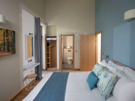A bedroom with a bed with blue and floral pillows a blue throw a wooden stool a wall mirror an open wardrobe and a bathroom Glentress Forest Silver Birch wheelchair accessible cabin Glentress Forest Peebles
