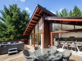 An outdoor deck with a round glass table and wicker chairs next to a hot tub and a wooden house with large windows at Delamere Forest White Willow Premium in Delamere Forest