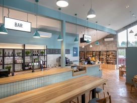 A bar and reception area with shelves of drinks and gifts and wooden tables and chairs at Delamere Forest Silver Birch in Delamere Forest