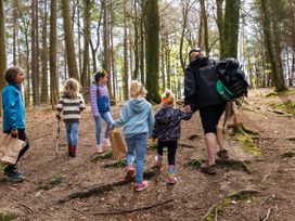 A forest with children and a forest ranger walking and carrying paper bags and sticks at Delamere Forest Silver Birch in Delamere Forest
