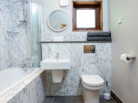 A bathroom with a bathtub shower combination a sink a toilet a round mirror and a window at Garwnant White Willow Premium Valley View Garwnant Bannau Brycheiniog Brecon Beacons