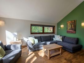 A living room with gray sofas and wooden coffee table near wooden side table with lamp and green accent wall with forest picture at Blackwood Forest Golden Oak in Blackwood Forest