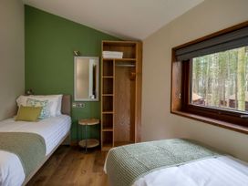 A bedroom with two single beds a wooden wardrobe a round side table and a window with a forest view at Blackwood Forest Golden Oak in Blackwood Forest