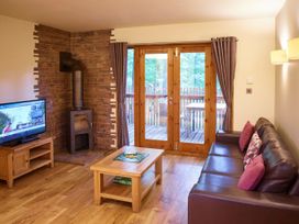 A living room with a leather sofa a wooden coffee table with a board game a wood stove a television and wooden doors leading outside at Sherwood Forest Golden Oak Sherwood Forest