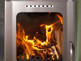 A close-up of a wood-burning stove with fire and logs inside at Delamere Forest Golden Oak in Delamere Forest
