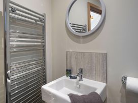 A bathroom with a wall-mounted sink a circular mirror a chrome towel radiator and a toilet paper holder at Delamere Forest Golden Oak in Delamere Forest