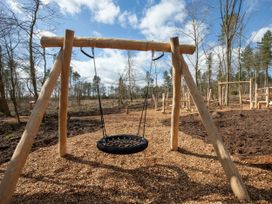 A wooden swing set with a black round swing in a forested playground at Delamere Forest Golden Oak in Delamere Forest