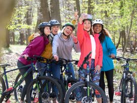 Five women with helmets on bicycles taking a selfie in a wooded area at Delamere Forest White Willow Premium in Delamere Forest