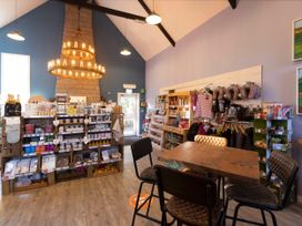 A retail shop interior with shelves of products a wooden table with four chairs under hanging lights at Beddgelert Golden Oak Hideaway Beddgelert Eryri Snowdonia