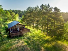 A cabin with large windows and a wooden deck surrounded by trees and grass at Cropton Golden Oak Hideaway in Cropton Forest