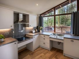 A kitchen with white cabinets a stainless steel sink and cooker under a large window showing trees outside at Garwnant Silver Birch wheelchair accessible cabin Garwnant Bannau Brycheiniog Brecon Beacons