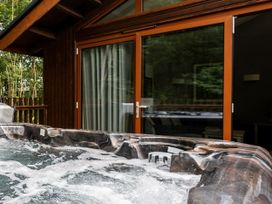A bubbling outdoor hot tub on a wooden deck outside a cabin with glass sliding doors at Glentress Forest White Willow Premium Valley View Glentress Forest Peebles