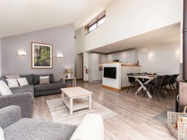 An open living room and dining area with grey sofas a wooden coffee table a dining table with black chairs and a kitchen in the background at Glentress Forest White Willow Premium Valley View Glentress Forest Peebles
