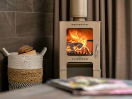 A wood burning stove with fire inside and a basket of firewood next to it at Glentress Forest White Willow Premium Valley View Glentress Forest Peebles