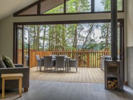 A living area with a sofa a wood stove and a wooden table with chairs on an open deck overlooking trees at Glentress Forest White Willow Premium Valley View in Glentress Forest Peebles