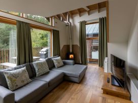 A living room with a gray sectional sofa pillows a wood stove television and large windows at Deerpark Classic Golden Oak Waterside in Deerpark Forest