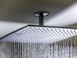 A ceiling-mounted square rain showerhead with water flowing at Glentress Forest Golden Oak Hideaway in Glentress Forest Peebles