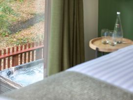 A bed next to a round wooden table with glasses and a bottle beside a window showing an outdoor hot tub at Forest of Dean Woodland - Golden Oak Treehouse in Forest Of Dean