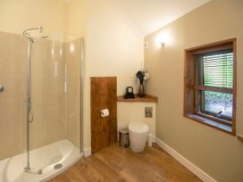 A bathroom with a glass shower enclosure a toilet a wooden window frame and a shelf with decorative items at Forest of Dean Woodland - Golden Oak Treehouse in Forest Of Dean