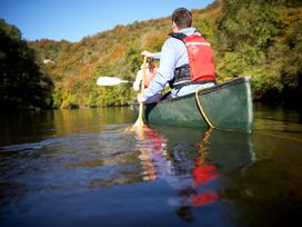 Two people paddling a green canoe on a river surrounded by trees with autumn foliage Forest of Dean Golden Oak Hideaway Forest Of Dean