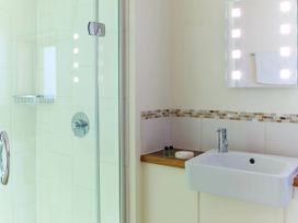 A bathroom with a glass shower enclosure a sink a lit mirror and toiletries on a wooden shelf at Ardgartan Argyll Silver Birch in Ardgartan Loch Long