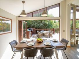 A dining room with a wooden table set for six people and large glass doors opening to an outdoor patio with chairs and a barbecue at Garwnant White Willow Premium in Garwnant Bannau Brycheiniog Brecon Beacons