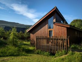 A wooden cabin with a fenced porch surrounded by grass and trees at Ardgartan Argyll Silver Birch wheelchair accessible cabin in Ardgartan Loch Long