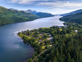 A cluster of cabins near a large river surrounded by hills and dense forest at Ardgartan Argyll Silver Birch wheelchair accessible cabin Ardgartan Loch Long