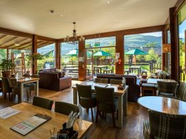 A dining area with tables chairs sofas and large windows overlooking an outdoor seating area with umbrellas at Ardgartan Argyll Silver Birch wheelchair accessible cabin in Ardgartan Loch Long
