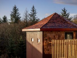 A wooden cabin with small windows and a fenced area surrounded by trees at Garwnant Golden Oak Treehouse Garwnant Bannau Brycheiniog Brecon Beacons