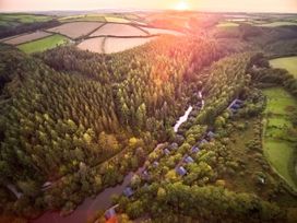 An aerial view of a forest with a river and small cabins near farmland at Deerpark Classic Golden Oak in Deerpark Forest