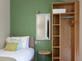 A bedroom with a single bed two pillows a wooden wardrobe with hangers and folded towels and a wall mirror at Forest of Dean Meadow - Golden Oak in Forest Of Dean