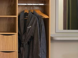 Three dark robes hanging on wooden hangers inside a wooden wardrobe next to a wall mirror at Forest of Dean Meadow - Golden Oak in Forest Of Dean