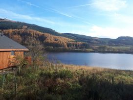 A wooden cabin near a lake with hills and trees in the background at Strathyre Golden Oak Lochside Strathyre Ben Ledi