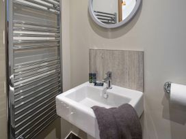 A bathroom sink with a faucet a towel on the sink a round mirror on the wall a chrome towel rack and a toilet paper holder at Cropton Silver Birch Compact in Cropton Forest