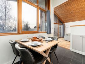 A dining area with a wooden table set for four and black chairs next to large windows in a room with a wooden ceiling at Cropton Silver Birch Compact in Cropton Forest