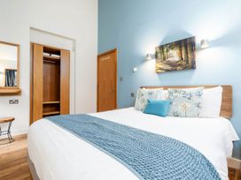 A bedroom with a bed with blue and floral pillows and a blue runner and wooden wardrobe with doors open at Cropton Silver Birch Compact in Cropton Forest