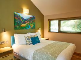 A bedroom with a bed wooden bedside tables and a window with blinds at Beddgelert Silver Birch - freshly inspired design wheelchair accessible cabin Beddgelert Eryri Snowdonia