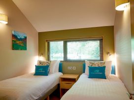 A bedroom with two single beds separated by a wooden nightstand and a window with blinds at Beddgelert Silver Birch - freshly inspired design wheelchair accessible cabin Beddgelert Eryri Snowdonia