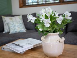 White flowers in a ceramic vase on a wooden table with books and a sofa in the background at Thorpe Forest Golden Oak Treehouse in Thorpe Forest