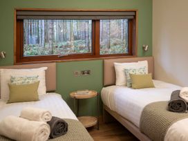 A bedroom with two single beds each with pillows and blankets and a window showing a forest view at Thorpe Forest Golden Oak Treehouse in Thorpe Forest